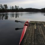 Getting back to the basics at Calm Waters Rowing A photo of a single rowing shell on still water, in the morning, alongside the dock at the training launch for Calm Waters Rowing.