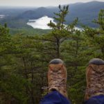 Practical gifts for the active traveler Hiking boots in the foreground and a treeline in the background, as if the photo was taken on the edge of a cliff.