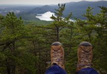 Practical gifts for the active traveler Hiking boots in the foreground and a treeline in the background, as if the photo was taken on the edge of a cliff.