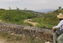 Camino de Santiago: Walking the French Way princess-style Woman sits on a stone fence and looks over a sprawling valley in Northern Spain, during her walk on the Camino de Santiago.