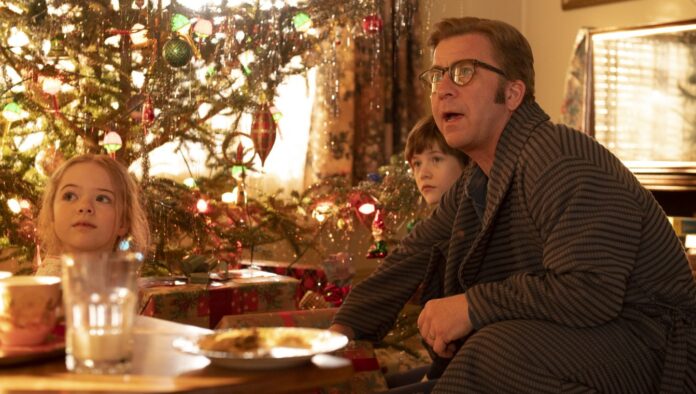 Peter Billingsley plays Ralphie, a father, sitting near a brightly-lit Christmas Tree with his young son and daughter.