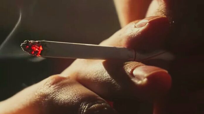 A close-up shot of someone taking a drag from a cigarette, with a glowing red tip.