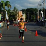 Fitting fitness in: Making yourself priority A woman is fitting fitness in by running in the final stretch of an organized race, with crowds of people along the side cheering the runners on.