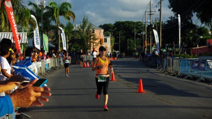 A woman is fitting fitness in by running in the final stretch of an organized race, with crowds of people along the side cheering the runners on.