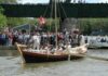 Quest for the Bay: Day 1 A large brown york boat with a mast and six rowers pushes away from a public dock where hundreds of people gather to watch the start of this unique and bizarre york boat voyage.