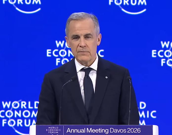 Prime Minister Mark Carney in a dark blue suit and tie, white shirt, and order of Canada pin on his lapel, addresses the audience from a podium on a stage, in front of a royal blue backdrop with'World Economic Forum' branding on it.