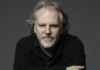Guy Maddin: One of Canada’s most extraordinary filmmakers Close-up shot of Guy Maddin, a distinguished looking man with thinning grey hair and goatee, wearing a black sweater, arms crossed in front, leaning into and looking into camera.